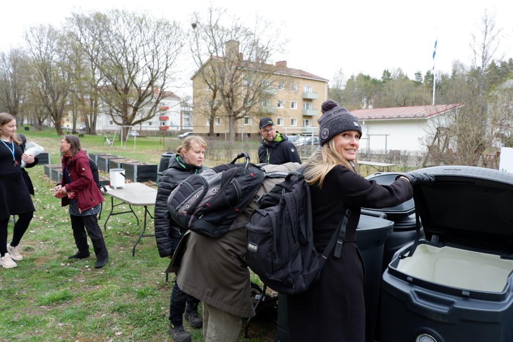 Ihmisiä ulkona roska-astioiden luona.